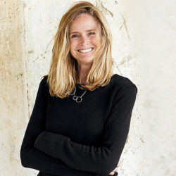 Annie pictured from the waist up smiling with her arms folded and hair blowing around, wearing a long sleeve black garment