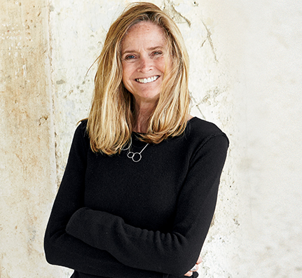 Annie pictured from the waist up smiling with her arms folded and hair blowing around, wearing a long sleeve black garment