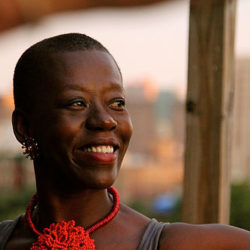 Headshot of Carmen pictured looking off to the right of the camera, wearing a red necklace with a large knotted pendant of beads